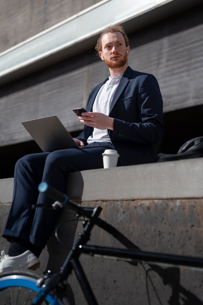 Photo homme assis à l'extérieur avec un ordinateur portable plein coup