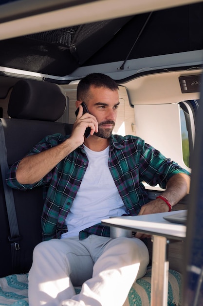 Homme assis à l'intérieur de son camping-car parlant au téléphone