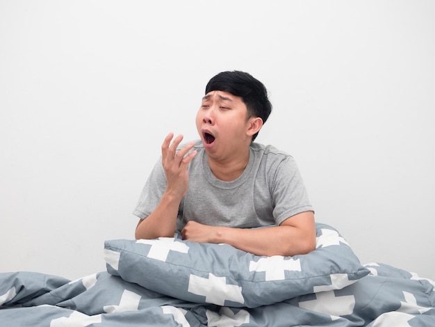 Un homme assis sur le lit avec un oreiller a sommeil et bâille