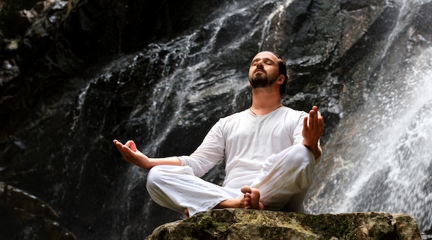 Homme assis en méditation yoga sur rocher à cascade