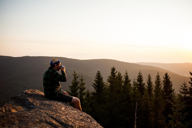 Un homme assis sur une montagne contre le ciel au coucher du soleil