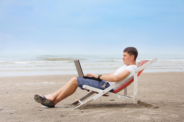 Photo homme assis sur une plage avec un ordinateur portable