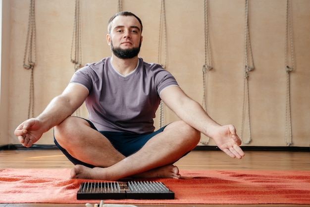 Photo homme assis en posture de lotus avec planche de sadhu en studio de yoga méditant