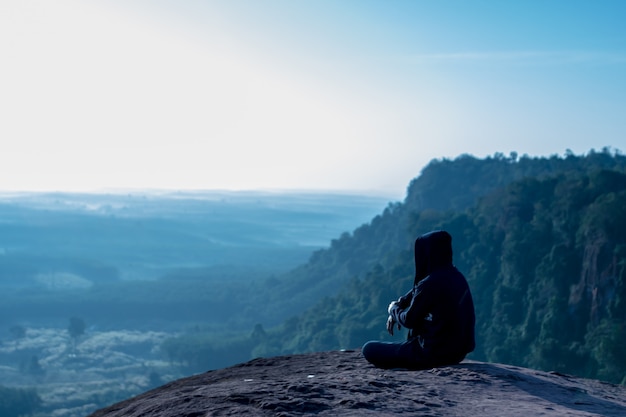 Homme assis et regardant le lever du soleil sur la falaise