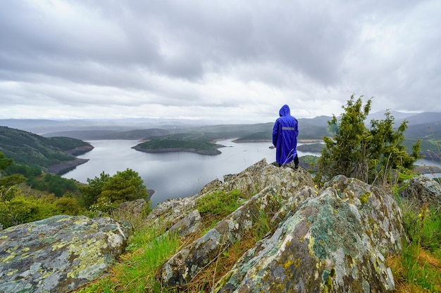 Homme assis sur un rocher dans les montagnes tout en contemplant le paysage avec un grand lac dans la vallée