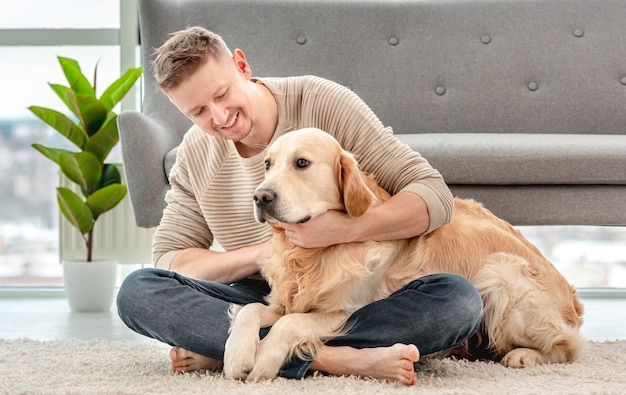 Homme assis sur le sol et étreignant un chien golden retriever. Propriétaire caressant son chien dans une pièce ensoleillée à la maison