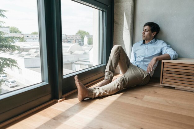 Homme assis sur le sol regardant par la fenêtre