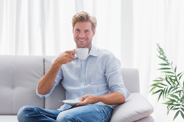 Homme assis sur son canapé à boire un café