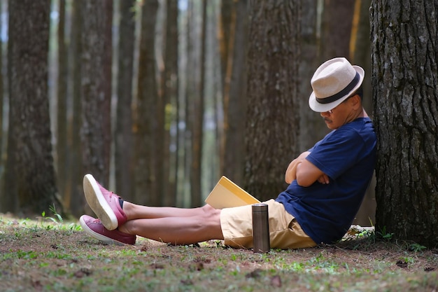 Un homme assis sous un arbre couvrant son visage avec un chapeau dormant