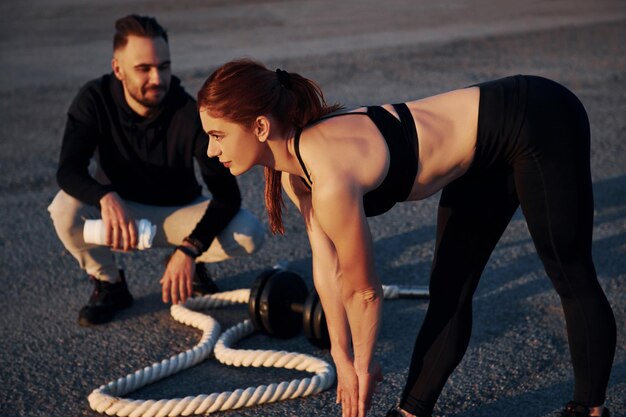 Homme assis et tenant une bouteille d'eau Femme et homme ont une journée de remise en forme sur la route le soir ensemble