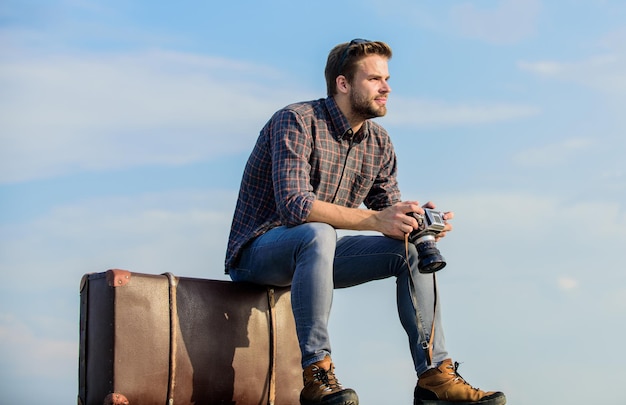 Homme assis sur une valise Concept de photojournaliste Blog de voyage Blogueur de voyage Beau mec voyageur appareil photo rétro Voyage avec bagages Tournage vlog Temps de vacances Guy à l'extérieur avec une valise vintage