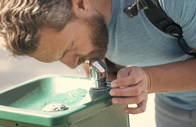 Un homme assoiffé boit de l'eau d'une fontaine à boire pour étancher sa soif d'hydratation