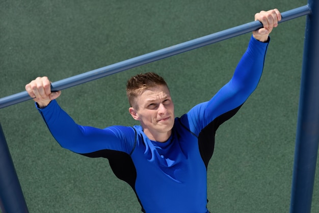 Photo homme athlète fort faisant pull-up sur barre horizontale sur le fond de l'herbe