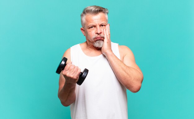 Homme athlète senior se sentant choqué et effrayé, l'air terrifié avec la bouche ouverte et les mains sur les joues