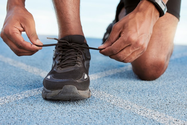Homme athlétique actif se préparant à une course d'entraînement pour augmenter l'endurance d'une course compétitive sur une piste olympique Gros plan d'un athlète afro-américain en forme attachant ses lacets avant de courir à l'extérieur