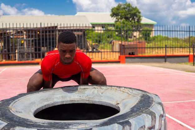 Homme athlétique africain soulevant un grand pneu de gym dans la salle de gym