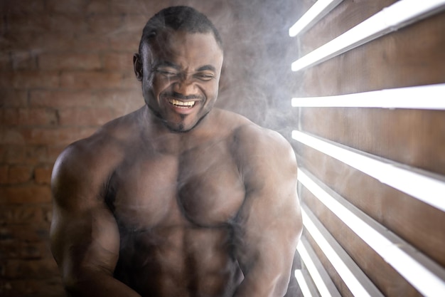 Homme athlétique afro-américain fort avec des muscles de forme parfaite sur fond de brique à côté des lampes à la lumière du jour