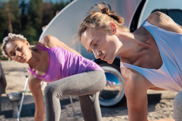 Homme athlétique. Athlétique bel homme aux cheveux blonds faisant du yoga avec sa petite amie attrayante