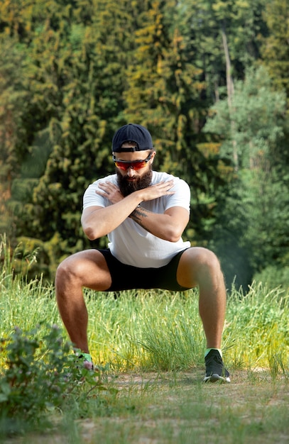 Homme athlétique barbu faisant de l'exercice dans la salle de gym en plein air au coucher du soleil.