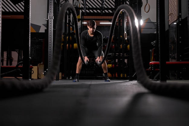 Homme athlétique faisant des exercices d'ajustement croisé avec une corde au gymnase, concentré et concentré sur la formation, l'entraînement. les gens et le sport, concept cross fit