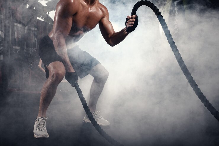 Photo homme athlétique faisant des exercices de crossfit avec une corde dans une salle de sport enfumée
