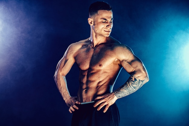 Homme athlétique fléchissant les muscles dans l'obscurité avec de la fumée. Bodybuilder fort avec des abdos parfaits.