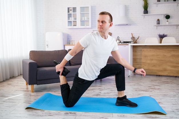 Homme athlétique musclé en t-shirt faisant des exercices d'échauffement à la maison. Faire du sport à la maison pendant la période de quarantaine. Remise en forme en dehors de la salle de gym