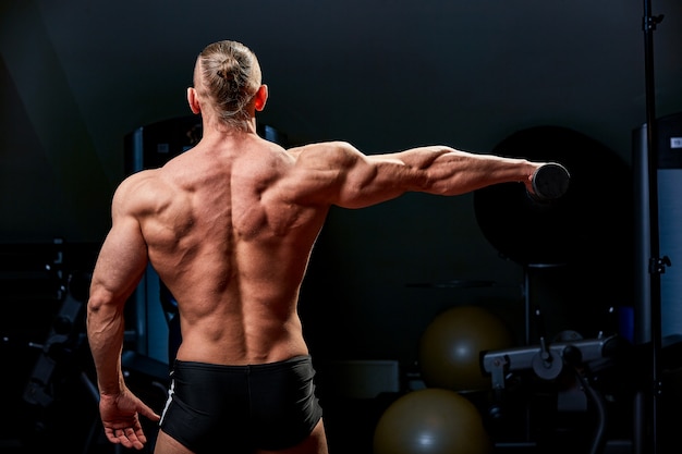 Homme athlétique posant. Photo d'un homme au physique parfait sur mur noir. Vue arrière. Force et motivation