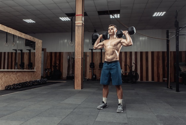 Homme athlétique puissant entraînant les muscles des épaules avec des haltères lourds dans la salle de sport