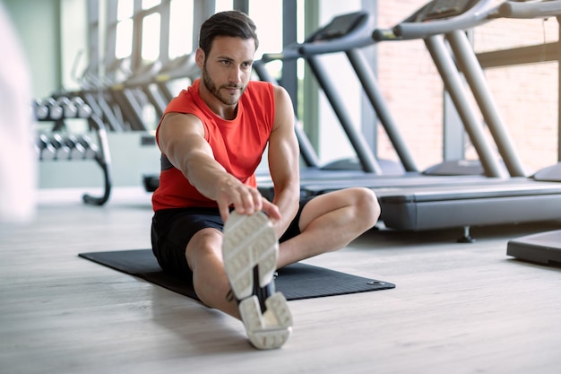 Homme athlétique s'étirant sur le sol tout en s'échauffant dans une salle de sport