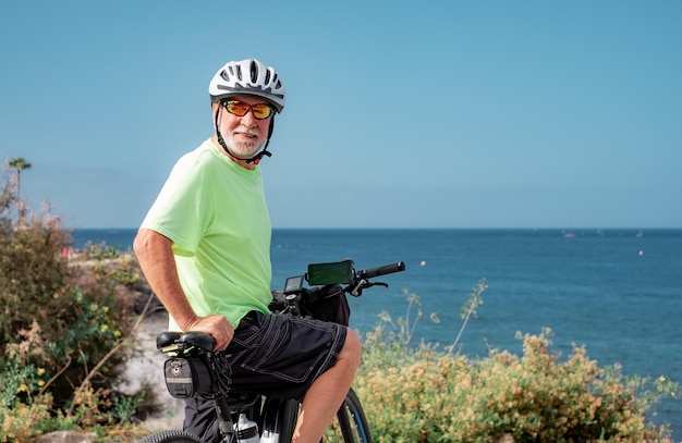 Homme athlétique senior avec vélo électrique en excursion en mer portant un casque profitant de la liberté