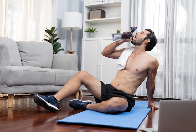 Un homme athlétique et sportif buvant de l'eau sur un tapis de fitness à la maison de gaieté