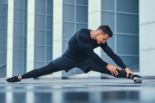 Un homme athlétique sportif s'échauffe et s'étire à l'extérieur sur fond de bâtiment moderne.