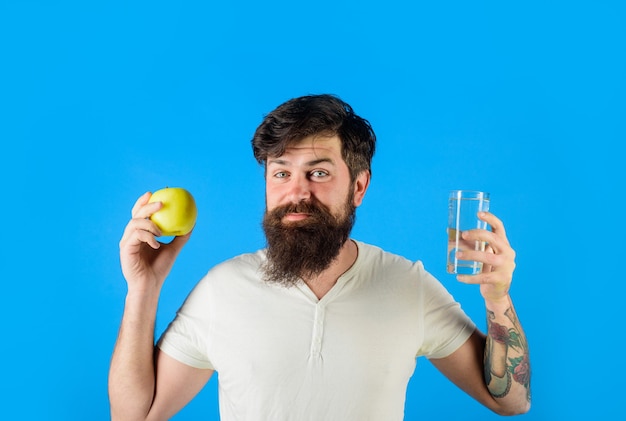 L'homme athlétique tient un verre d'eau et une pomme Un bel homme barbu tient une pomme verte et un verre de