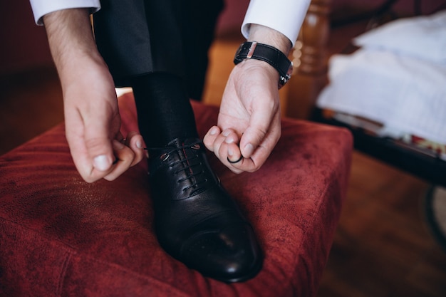 Homme attachant les lacets sur des chaussures noires sur un plancher en bois