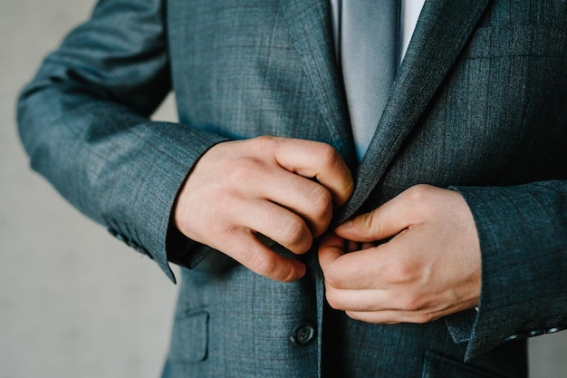 L'homme attache les boutons Le marié dans une cravate de chemise de costume est debout sur fond gris Gros plan