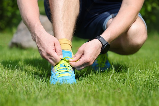 L'homme attache des lacets sur des baskets bleu vif homme accroupi sur l'herbe dans le concept de parc