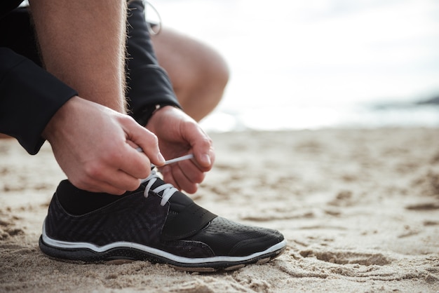 L'homme attache des lacets en se tenant debout sur le sable Gros plan