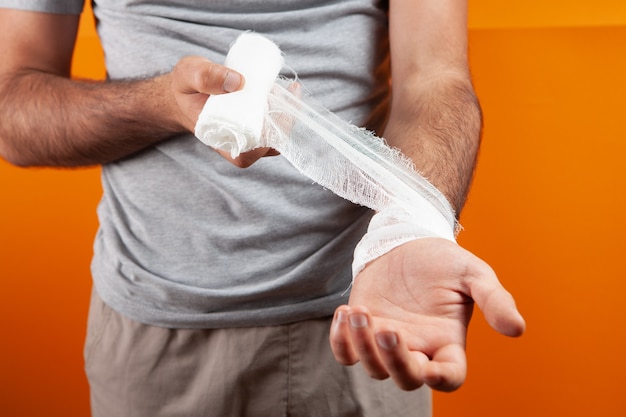 L'homme a attaché sa main avec un bandage sur un fond orange