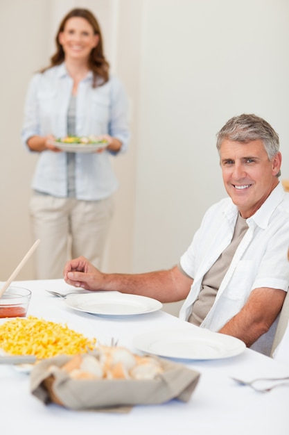 Un homme attend sa femme pour apporter de la salade à la table