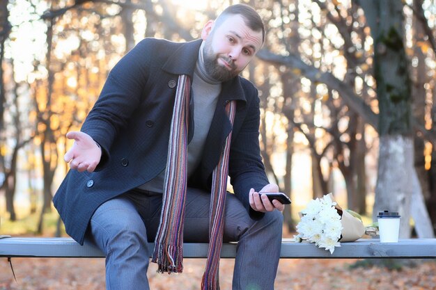 Homme attendant sur un banc la date en automne parc avec fleur