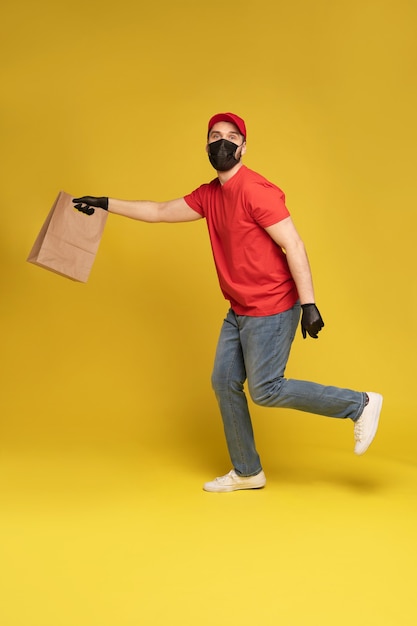Homme au bonnet rouge, t-shirt en masque de protection et gants donnant l'ordre de restauration rapide isolé sur mur jaune