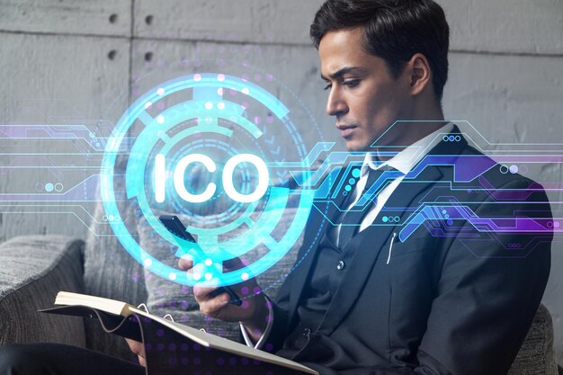 Un homme au bureau prenant des notes à l'aide d'un téléphone et d'un hologramme de thème blockchain ico