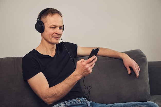 L'homme au casque et avec un smartphone est assis sur le canapé