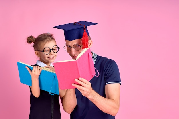 Homme au chapeau académique tenant un livre, étudier avec une jolie fille préadolescente en uniforme scolaire