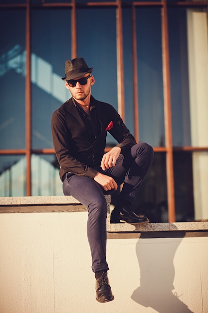 Homme au chapeau et lunettes de soleil posant dans la ville.