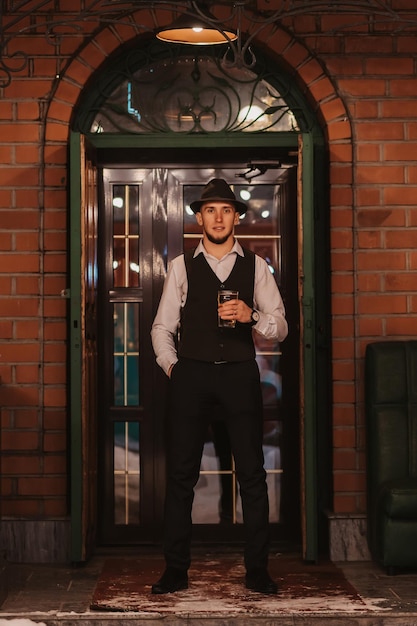 L'homme au chapeau se tient avec un verre de bière à la main à la porte du bar