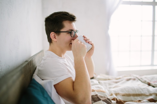 Homme au lit, boire du café du matin à la lumière du lever du soleil.