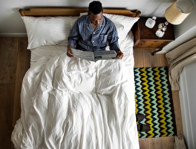 Homme au lit en lisant un journal