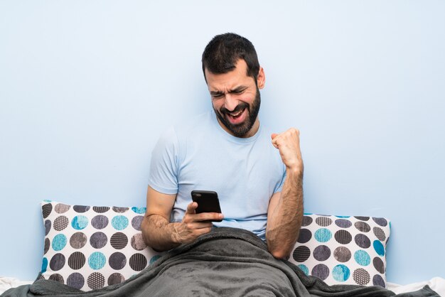 Homme Au Lit Avec Téléphone En Position De Victoire